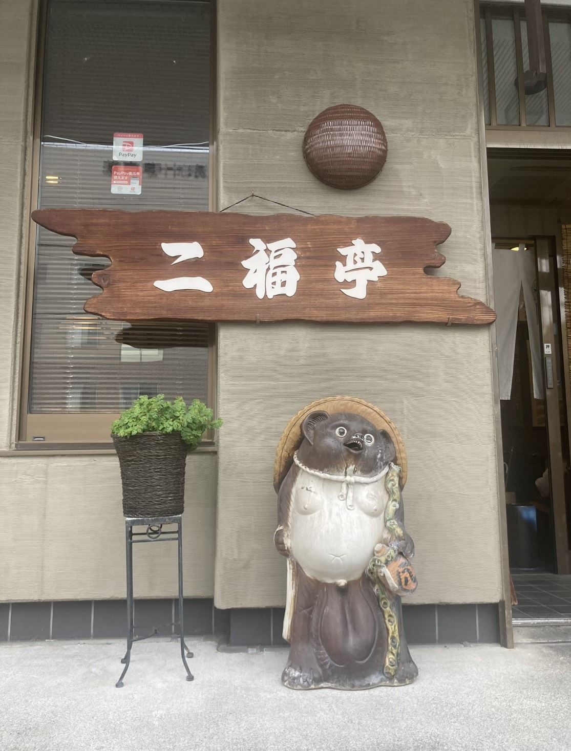 木彫りの二福亭の看板と、店先に置かれたたぬきの置物